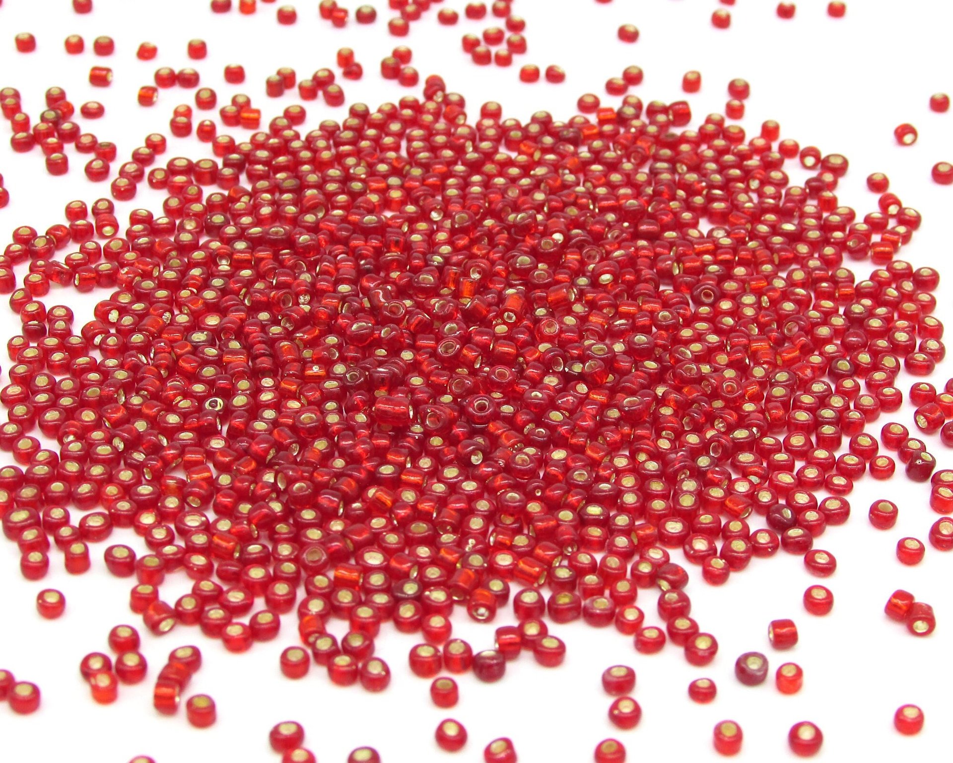 8/0 seed beads are translucent red mini rocailles with a gold foil lining. Beads average 2.5x3.5mm with round 1.0mm holes. There are approximately 38-40 beads per gram.