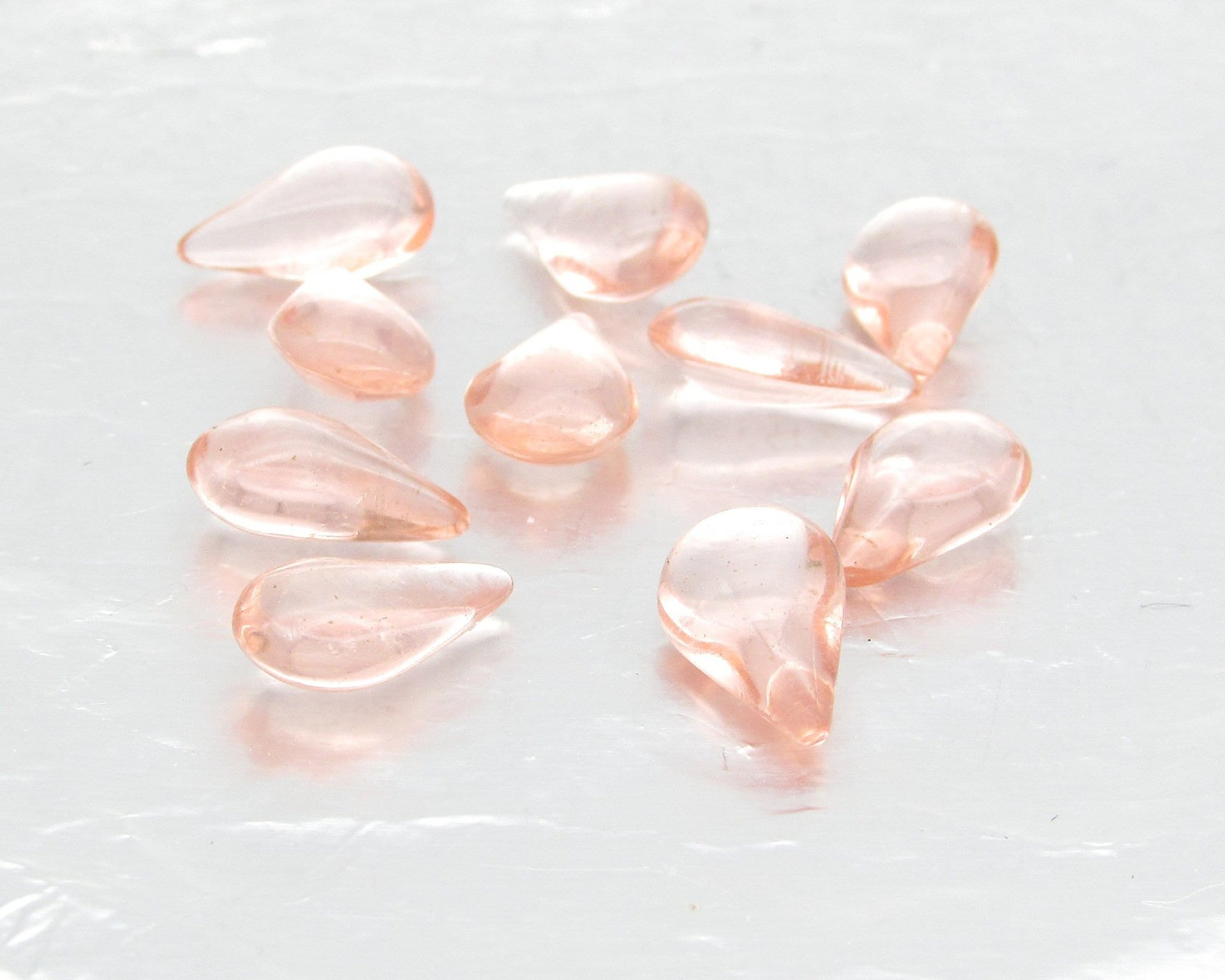 Vintage glass teardrop cabochons are translucent pale pink. Pressed glass stones measure 12.8mm long, 7.8mm wide, and  4.5mm thick at the center. The unfoiled backs come to a soft point.